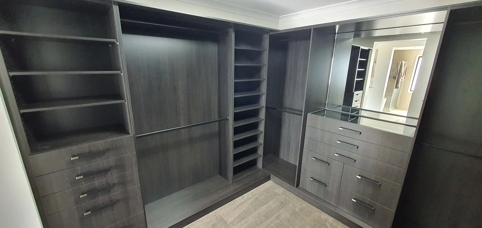 Dark timber walk-in wardrobe with shelving, drawers and dressing mirror